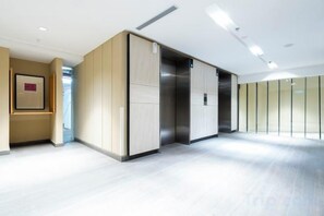 A modern elevator with a metallic finish, a light-colored wall with a framed picture, and a glass partition on the right. - Harmony Luxury Suites At Lucentia Bukit Bintang City Center (Kuala Lumpur)