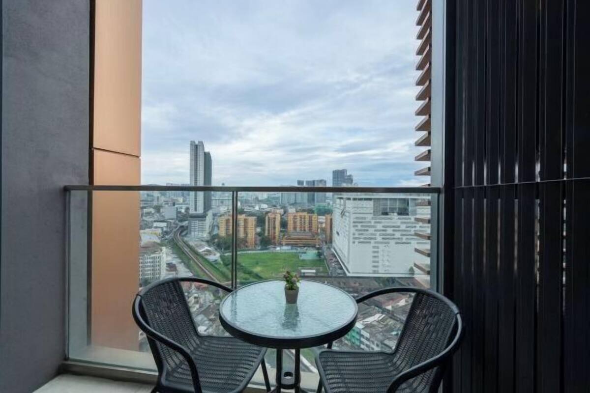 Ein Balkon mit Glastisch und Stühlen, mit Blick auf eine Stadtlandschaft mit Gebäuden und Grünflächen.
