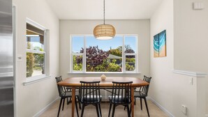 A dining area with a wooden table and black chairs, a hanging light fixture, and a window with a view of greenery. - Sleeps 8 in the Jewell Box close to Privates and Pleasure Point (Santa Cruz)