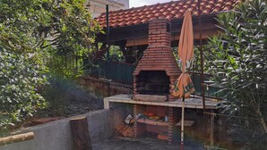 Un horno de ladrillo al aire libre con chimenea, rodeado de vegetación y una estructura de concreto.