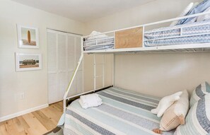 Una camera con un letto a castello, copripiumino a righe, un asciugamano bianco e cuscini. C'è un pannello di legno sul letto superiore e un armadio con ante a persiana.