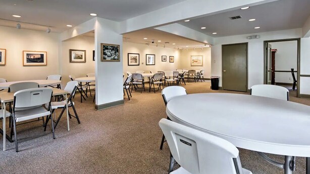 Une salle de conférence avec des tables et des chaises blanches, des œuvres d’art encadrées aux murs et un sol recouvert de moquette.