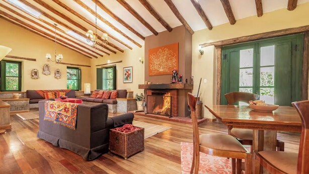 Amplia sala de estar con chimenea, vigas de madera, comedor y ventanas grandes.