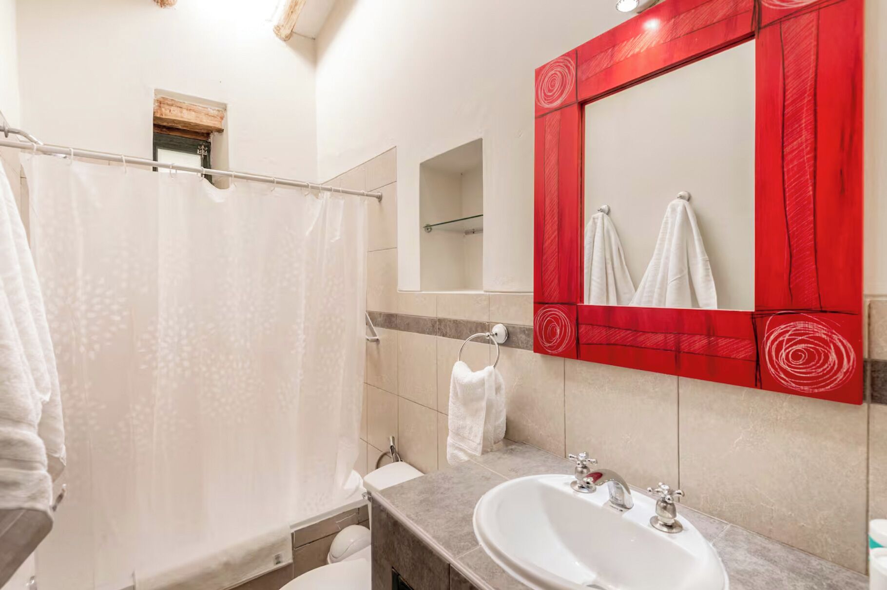Un baño con ducha, lavamanos, espejo y toallero.