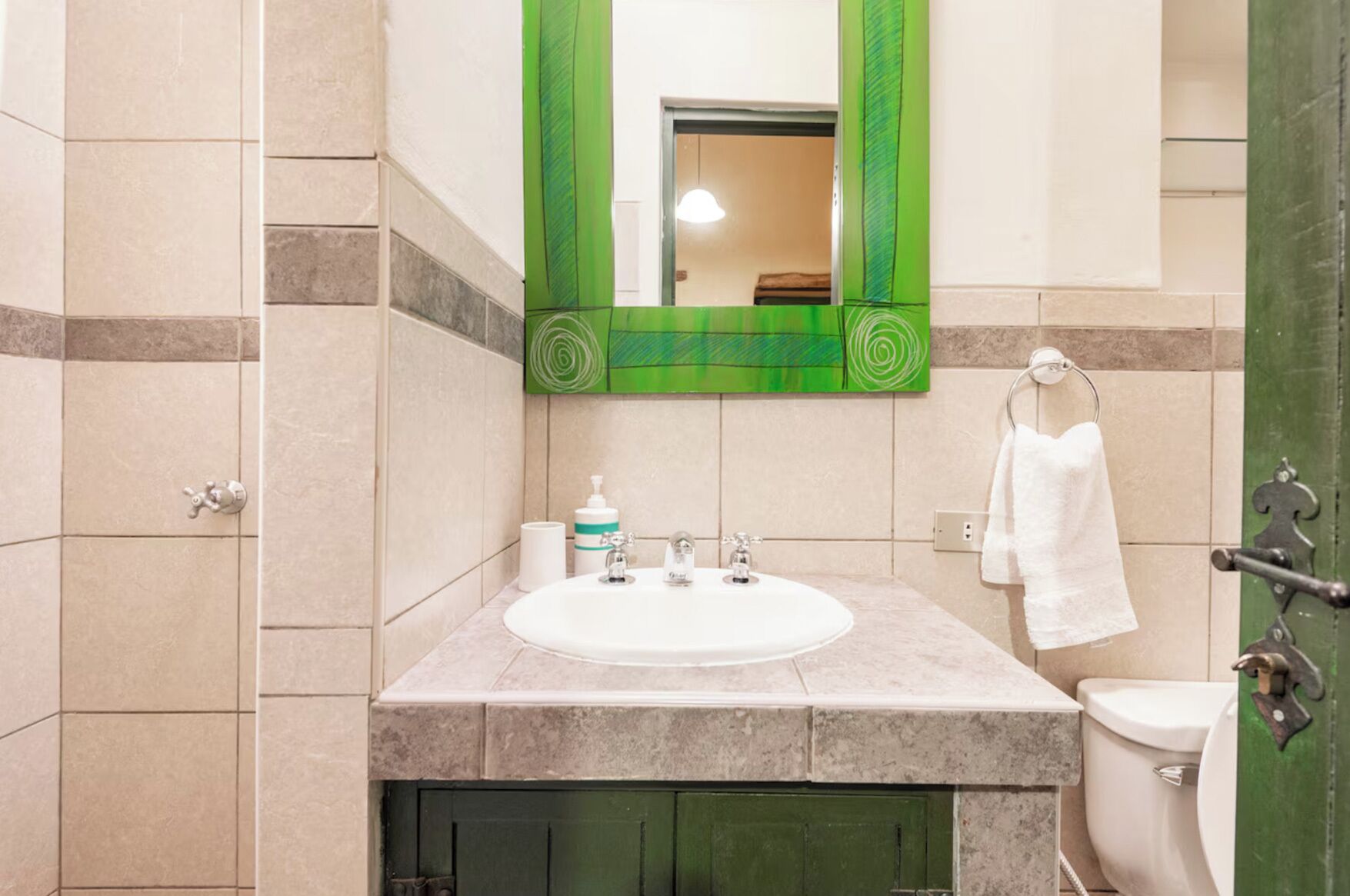 Une salle de bain avec un miroir à cadre vert, un lavabo blanc, des toilettes et un porte-serviettes.