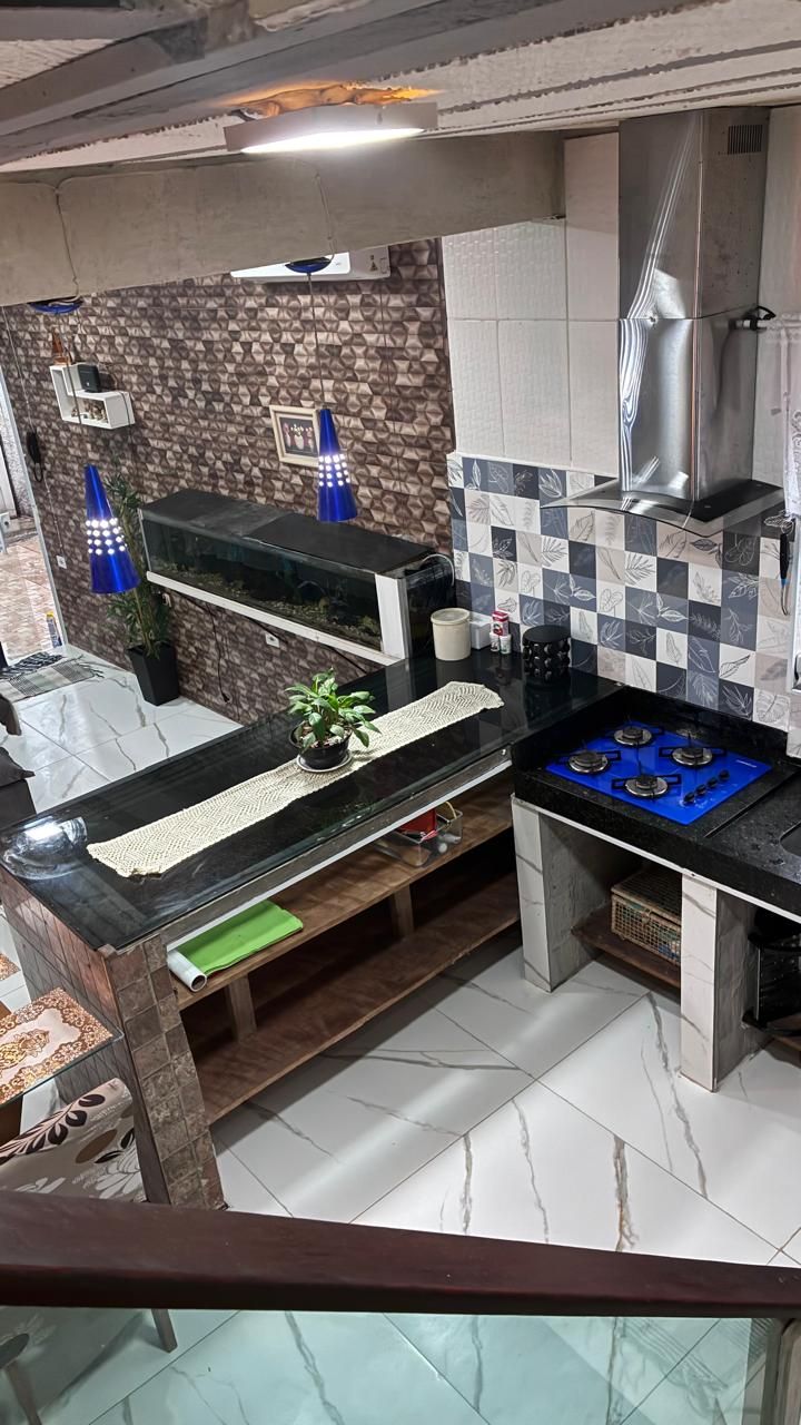 A kitchen with a black countertop, a blue gas stove, a stainless steel range hood, and a patterned backsplash.