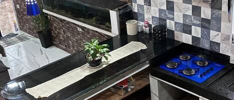 A kitchen with a black countertop, a blue gas stove, a stainless steel range hood, and a patterned backsplash.