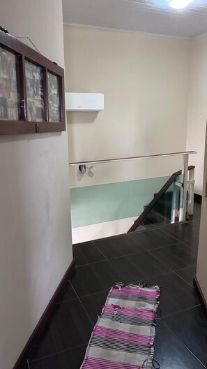 A staircase with a glass railing, a dark floor, and a patterned rug. - Townhouse with pool and air conditioning near Caraguatatuba shopping mall (Caraguatatuba)