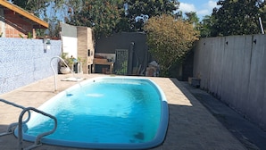 A rectangular swimming pool with a tiled edge, surrounded by a concrete deck and a low brick wall. - Townhouse with pool and air conditioning near Caraguatatuba shopping mall (Caraguatatuba)