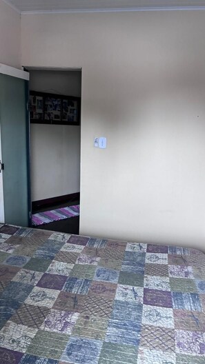 A room with a checkered floor, a door leading to a room with a bed and a wall-mounted shelf. - Townhouse with pool and air conditioning near Caraguatatuba shopping mall (Caraguatatuba)
