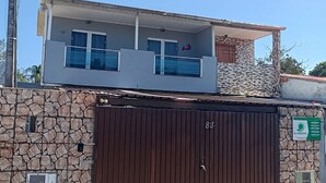 A two-story house with a stone facade, a brown gate, and a balcony with a railing. - Townhouse with pool and air conditioning near Caraguatatuba shopping mall (Caraguatatuba)