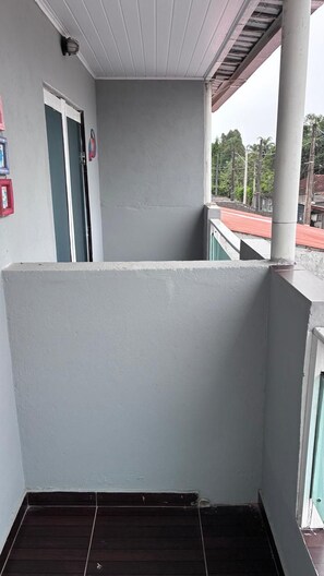 A balcony with a white railing, a door, and a view of a red-roofed building. - Townhouse with pool and air conditioning near Caraguatatuba shopping mall (Caraguatatuba)