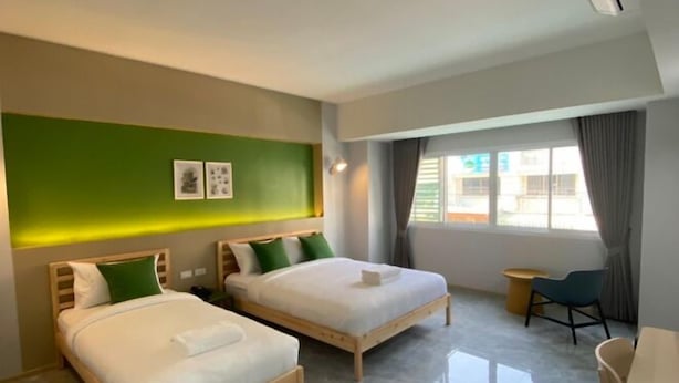 A modern hotel room with two beds, a small desk, and a window with curtains.