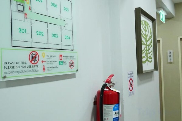 Sinal de segurança contra incêndio com indicações de saída de emergência e um extintor fixado na parede.