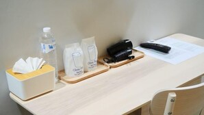 A neatly arranged desk with a tissue box, two glass containers, a water bottle, a black phone, a remote control, and a document.