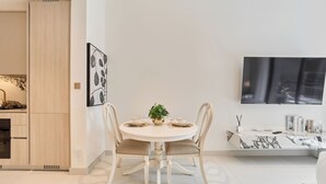 Un'area pranzo moderna con un tavolo rotondo, due sedie, una pianta in vaso e un televisore a schermo piatto montato a parete.