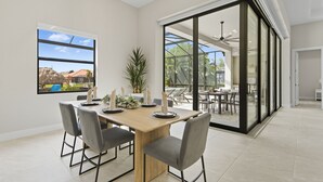 Un comedor moderno con una mesa de madera, sillas grises y un amplio ventanal con vistas a un jardín.