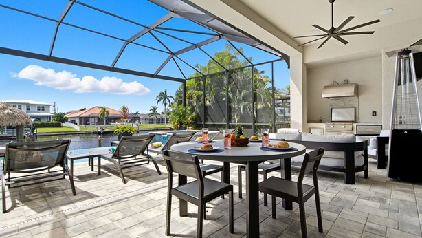 Un amplio patio exterior con cerramiento de vidrio, una mesa redonda de comedor y muebles de jardín modernos.
