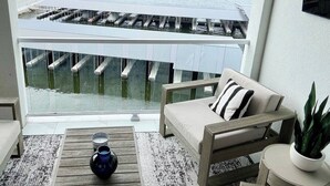 Un balcon donnant sur un pont enjambant une étendue d’eau, un canapé, une table basse et une plante en pot.