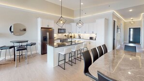 Une cuisine moderne dotée d’un îlot central, d’appareils électroménagers en acier inoxydable et de luminaires suspendus.