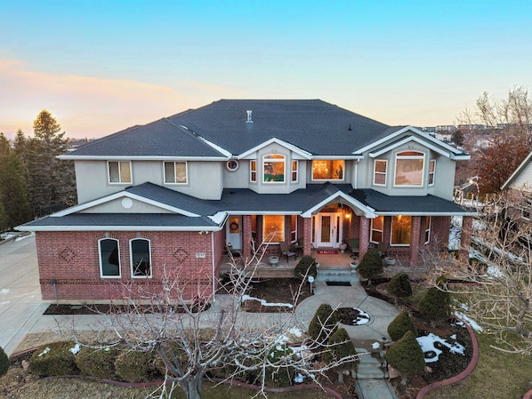 A two-story house with a brick facade, a front porch, and a covered entryway. - Mountain View Chateaux - A Lavish Mountain Retreat - Perfect for Large Families (Layton)