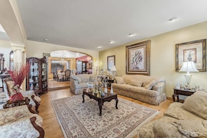 A spacious living room with a large coffee table, two sofas, and a patterned rug. There are framed pictures on the walls and a chandelier hanging from the ceiling. - Mountain View Chateaux - A Lavish Mountain Retreat - Perfect for Large Families (Layton)