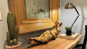 Ein Holztisch mit einer großen, gedrehten Astskulptur, einem Topf mit Kaktus und einer Schreibtischlampe.