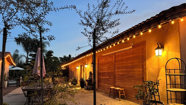 Ein Holzhaus mit einer Terrasse, Blumentöpfen und Lichterketten.