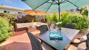 Eine Terrasse im Freien mit Esstisch, Stühlen und einem großen Sonnenschirm.