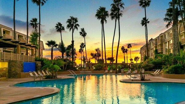 Une piscine bordée de palmiers, avec un coucher de soleil en arrière-plan.