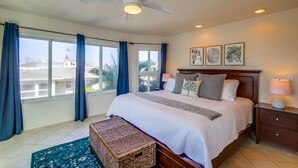 Un dormitorio amplio con una cama grande, un ventilador de techo y vistas de la ciudad a través de amplias ventanas.
