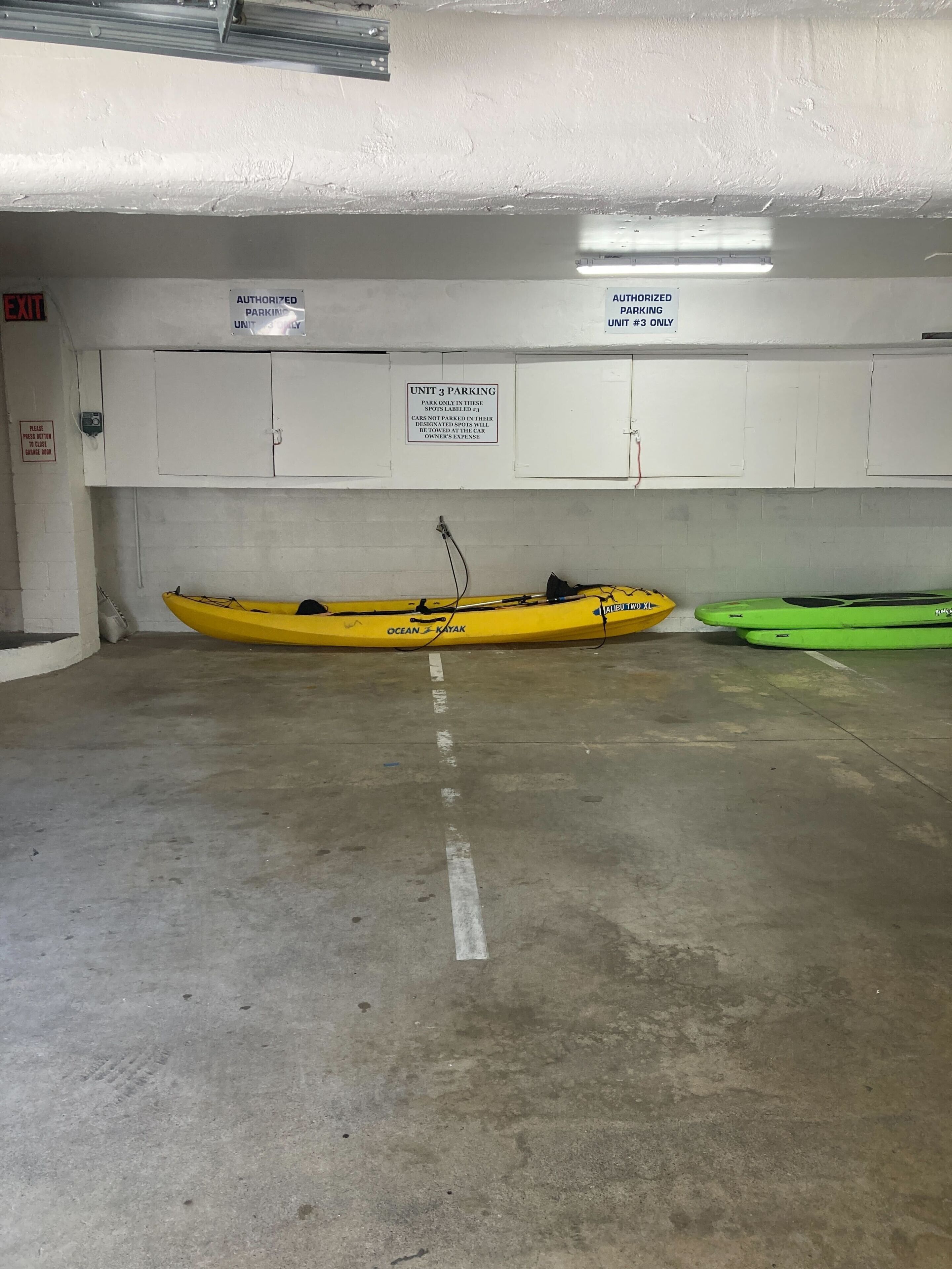 Eine Tiefgarage mit zwei Kajaks, einem gelben und einem grünen, und Schildern, die eine genehmigte Parkzone für Einheit 3 kennzeichnen.