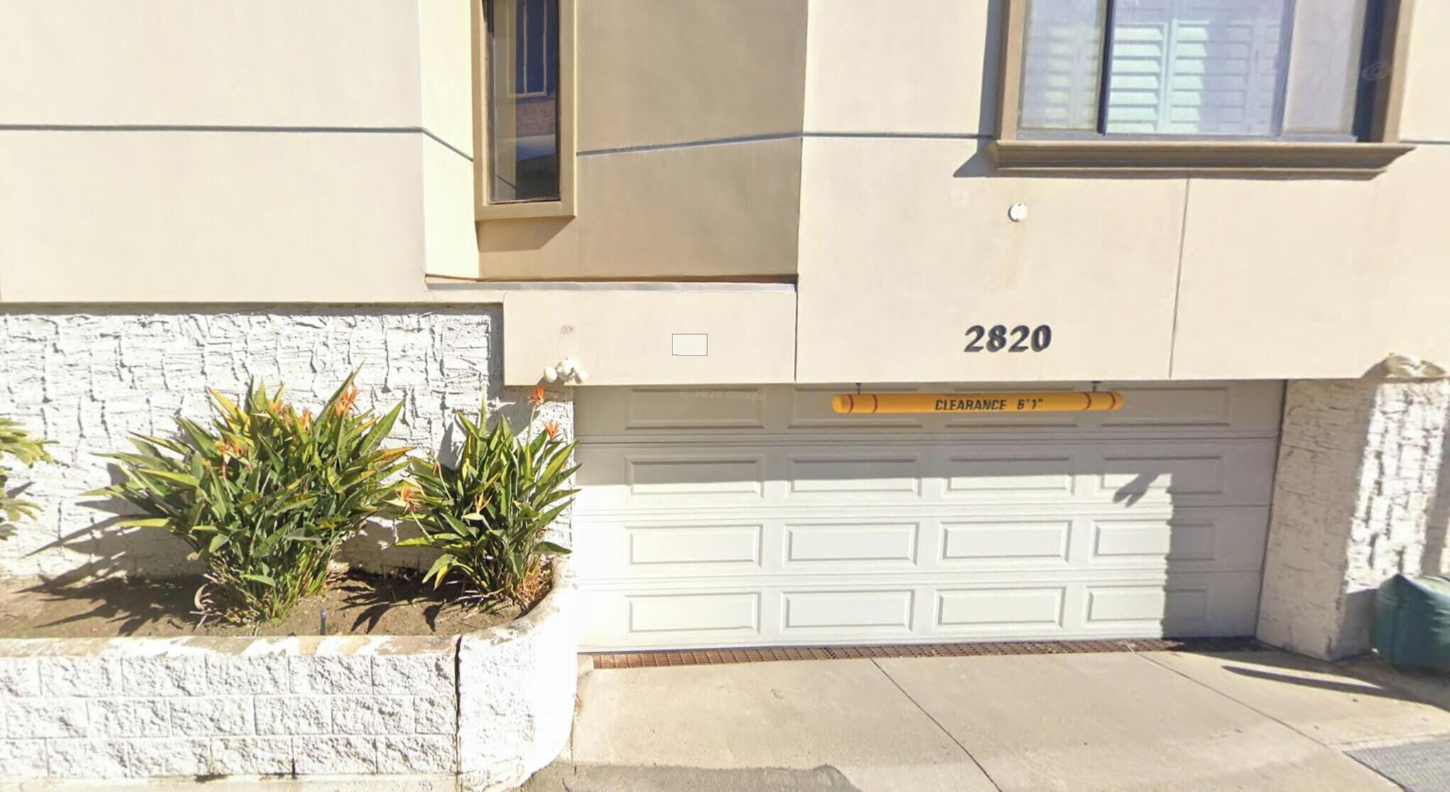 Un garaje residencial con un letrero de altura libre, una puerta de garaje blanca y el número 2820 en la pared.