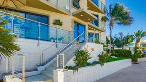 Un edificio de varios pisos con una escalera que conduce a la entrada, rodeado de palmeras y vegetación.