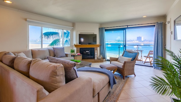 Una sala de estar con sofá, televisión, chimenea y vista al mar.