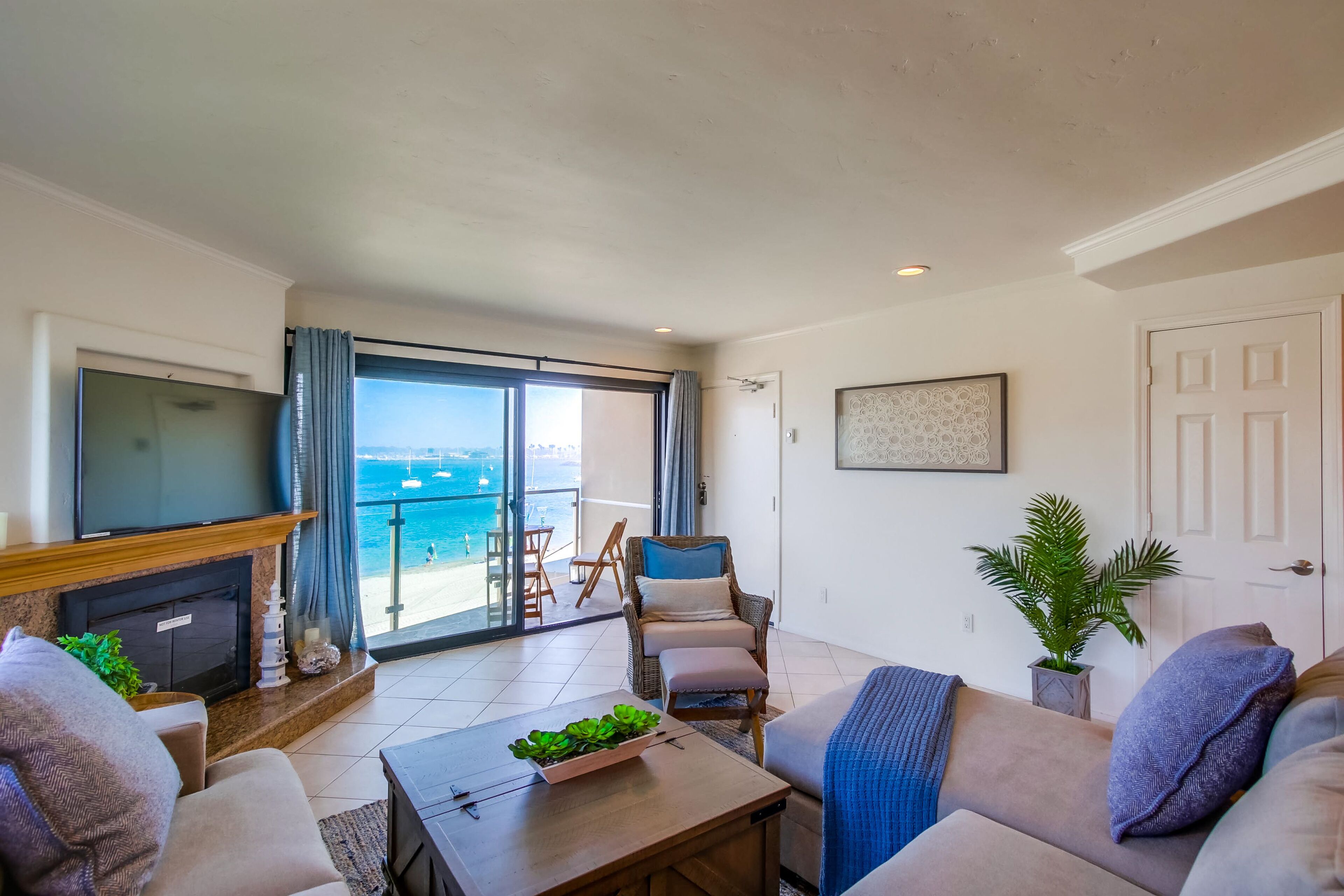 A living room with a TV, sofa, coffee table, and a view of the sea through a sliding glass door.