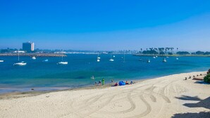 Una playa con barcos en el agua, gente en la arena y un edificio al fondo.