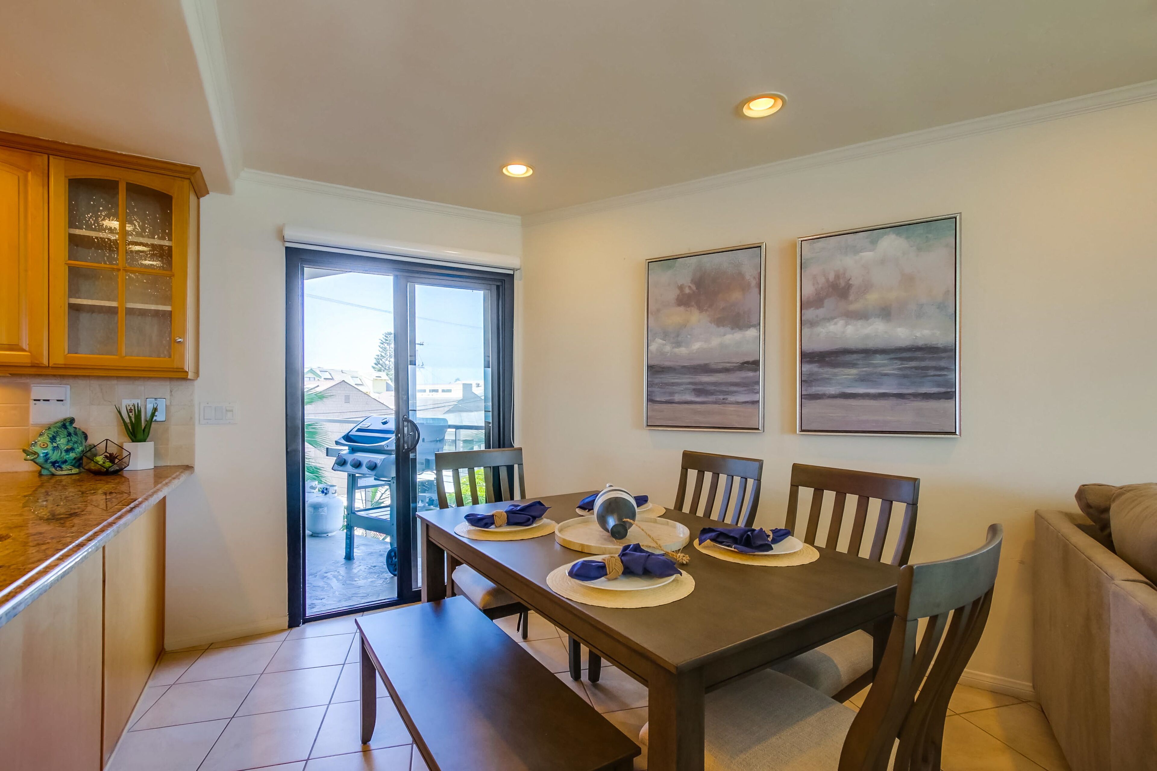 A dining area with a table set for four, a bench, and a view through a glass door to the outside.