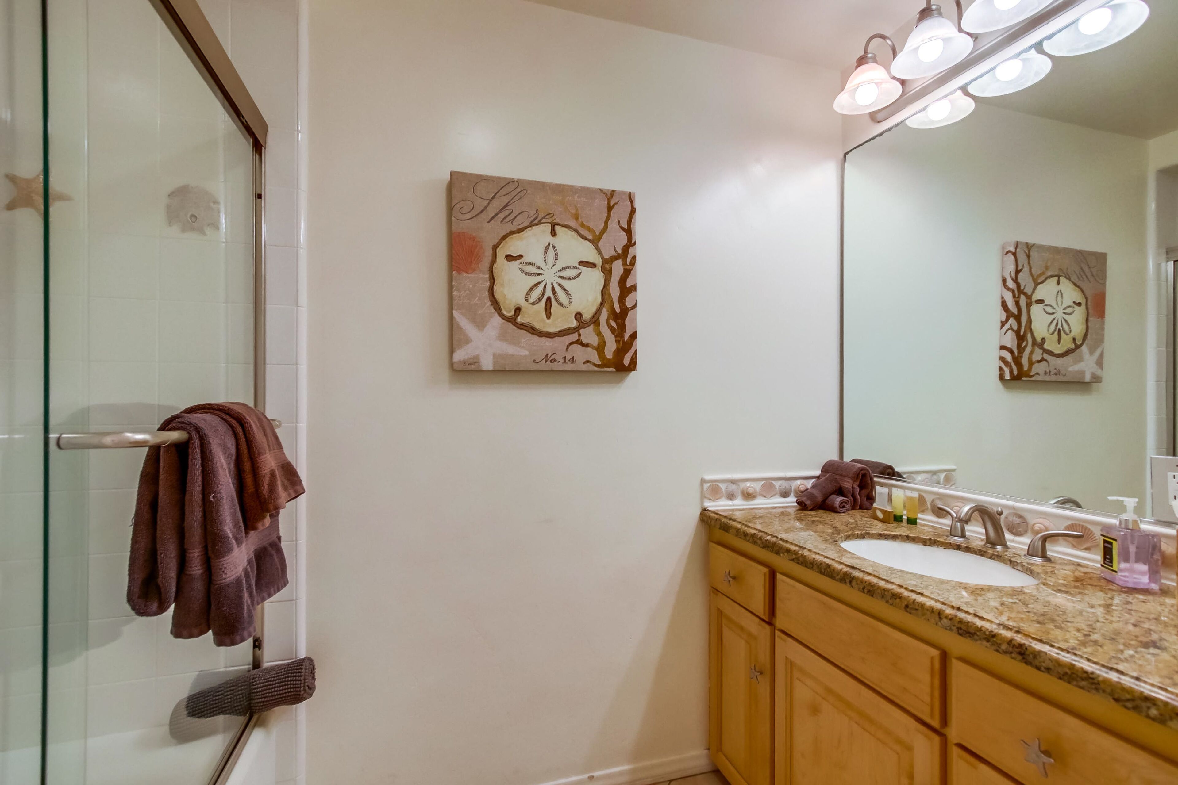 Une salle de bain avec une porte de douche en verre, un lavabo avec un meuble-vasque et un miroir fixé au mur.