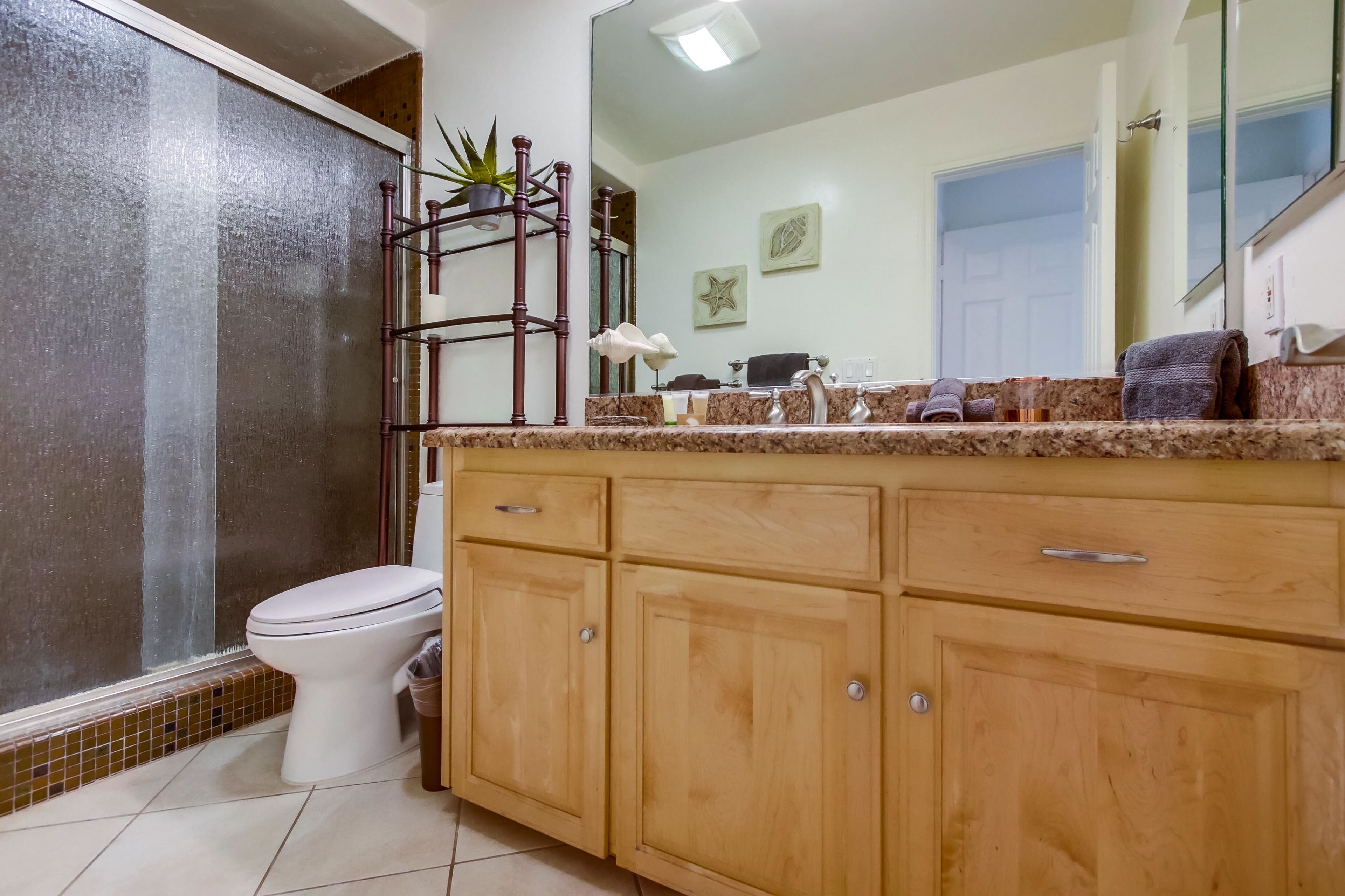A bathroom with a toilet, wooden cabinets, a marble countertop, a sink, and a mirror.