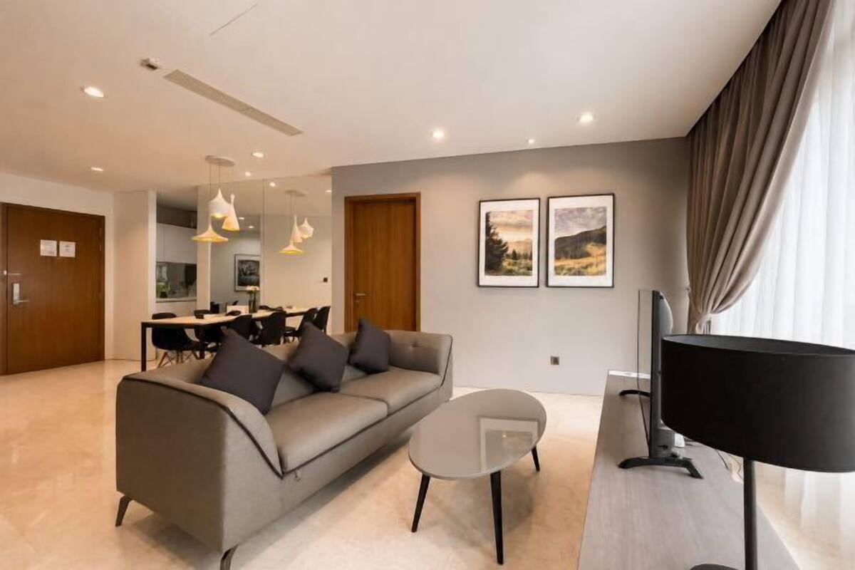 Un salon moderne avec un canapé, une table basse, un téléviseur et, au fond, un coin repas.
