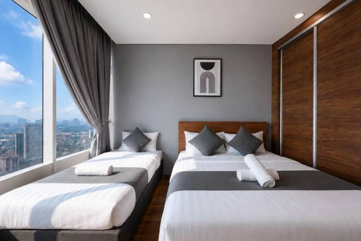 Une chambre d’hôtel avec deux lits, une grande fenêtre donnant sur la ville et un tableau encadré au mur.