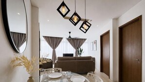 Een eethoek met een glazen tafel, stoelen, een vaas met gedroogde planten en een hanglamp.