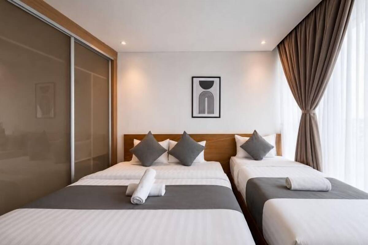 Une chambre d’hôtel avec deux lits, une porte coulissante, une œuvre d’art encadrée au mur et une fenêtre avec des rideaux.