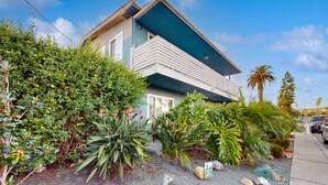 A modern two-story house with a balcony, surrounded by lush greenery and a clear blue sky. - Pacific Beach Cottage (San Diego)