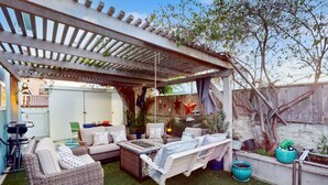 A covered patio area with wicker furniture, a hanging swing, and a pergola. - Pacific Beach Cottage (San Diego)