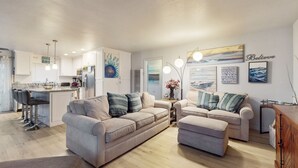 A modern kitchen with white cabinets, a central island with bar stools, and a dining area with two sofas and a coffee table. - Pacific Beach Cottage (San Diego)