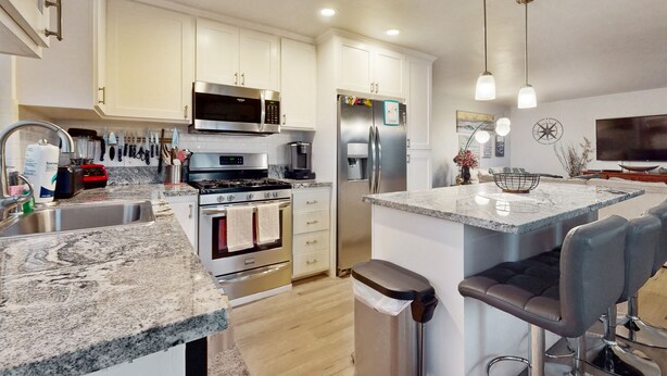 A modern kitchen with white cabinets, stainless steel appliances, a granite countertop, and a bar area with stools. - Pacific Beach Cottage (San Diego)