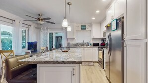 A modern kitchen with a marble countertop, stainless steel appliances, and a ceiling fan. - Pacific Beach Cottage (San Diego)