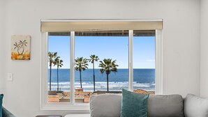 Ein Wohnzimmer mit großem Fenster und Meerblick, einer Couch mit Kissen und einem kleinen Tisch.